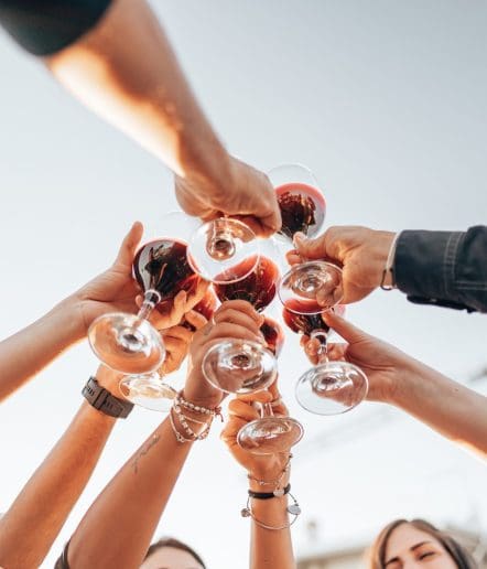 A group of people raising and clinking wine glasses in a toast under a clear sky, photographed from below—capturing the spirit of Paso Robles events.