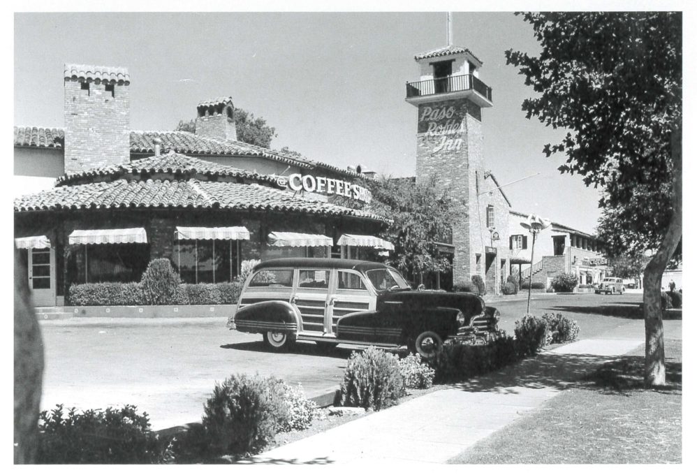Black and white photo of a vintage station wagon parked in front of the Paso Robles Inn, featuring a tall clock tower and a large building with a tiled roof and signage that reads “COFFEE SHOP.” Trees and shrubs line the sidewalk.