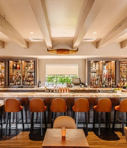 A stylish bar with brown leather barstools, a marble countertop, shelves of liquor bottles, and a decorative longhorn above the bar. Warm lighting and a window provide a welcoming atmosphere typical of Paso Robles Restaurants.
