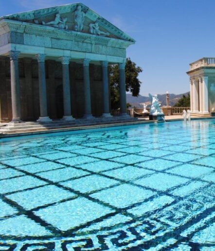 A clear blue swimming pool with geometric tile patterns sits in front of a grand, white Greco-Roman style pavilion—an elegant spot to unwind and enjoy unique Paso Robles activities under a sunny sky.