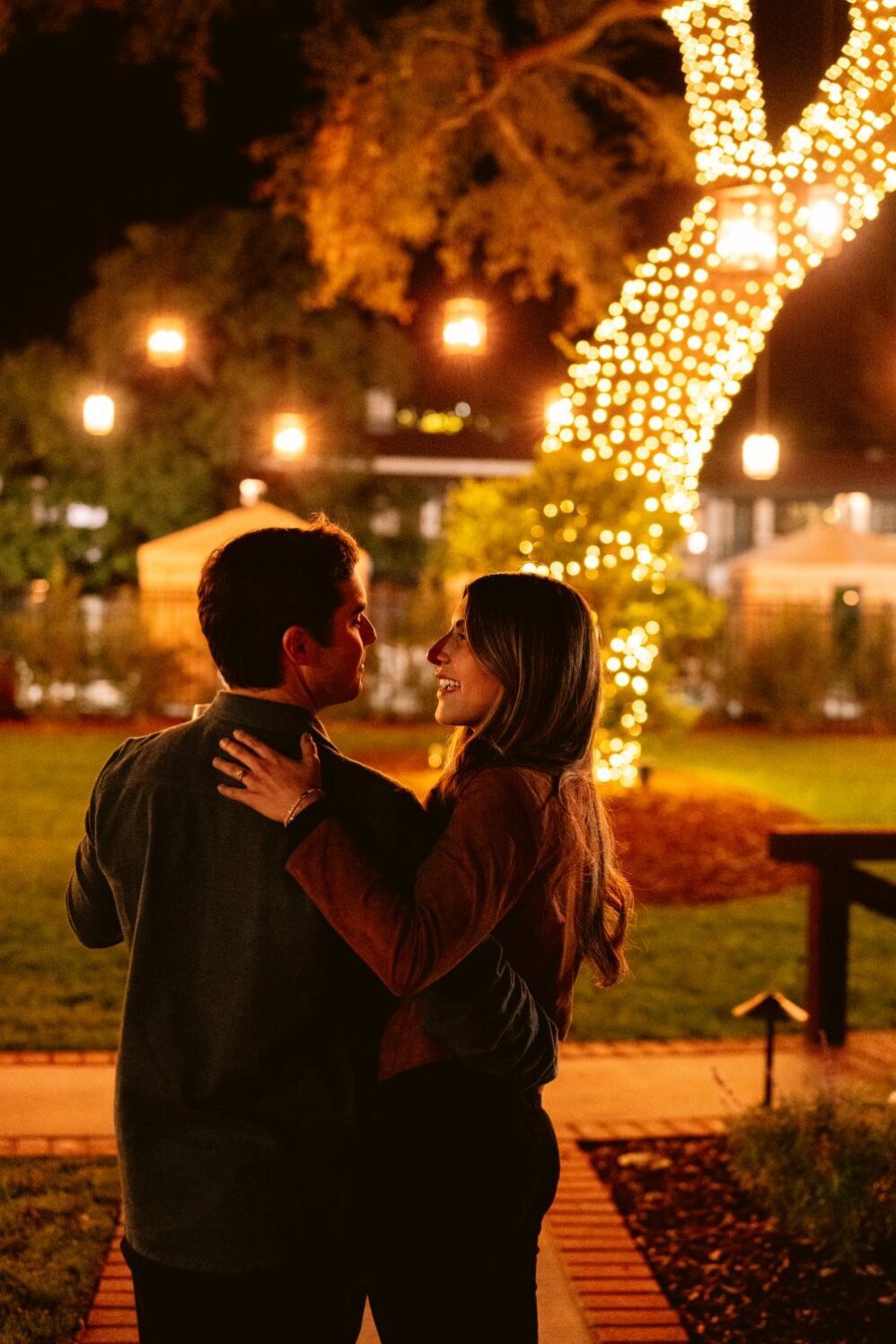couple hugging outside with lights on tree