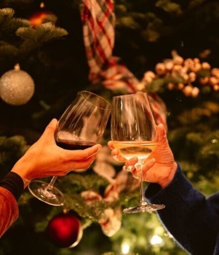 Two people clinking wine glasses—one red, one white—in front of a decorated Christmas tree, echoing the festive spirit found in Paso Robles restaurants during the holiday season.