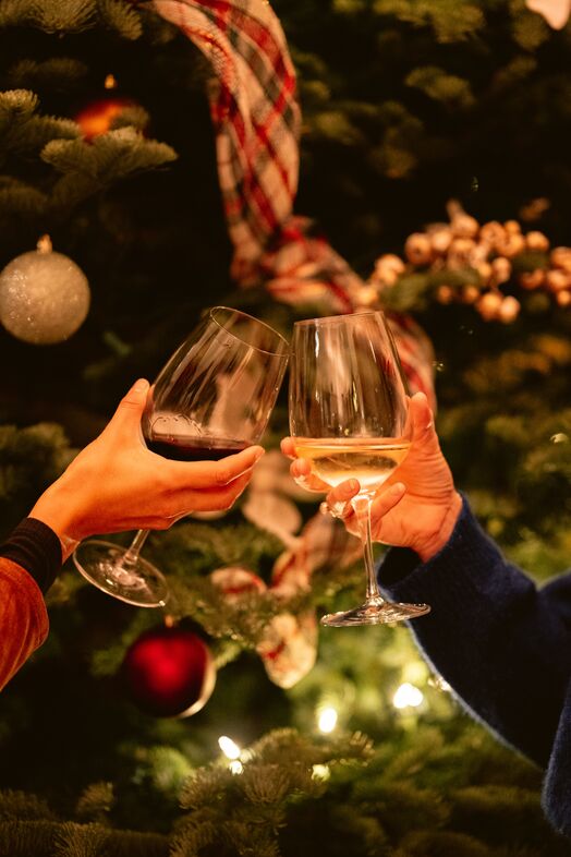 Wine glasses clinking in front of Christmas tree