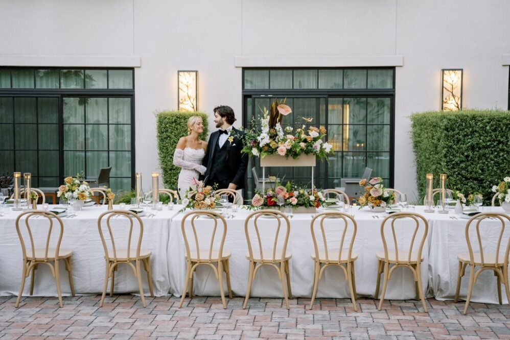 Bride and Groom standing behind long table with wooden chairs