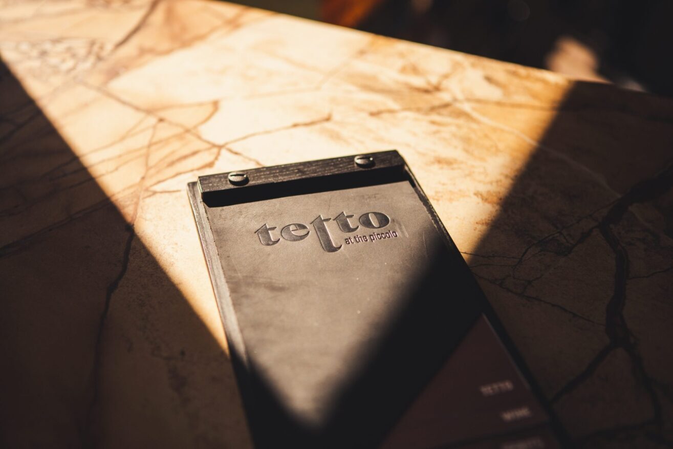 A restaurant menu labeled tetto lies on a marble surface, with sunlight and shadows partially covering it.