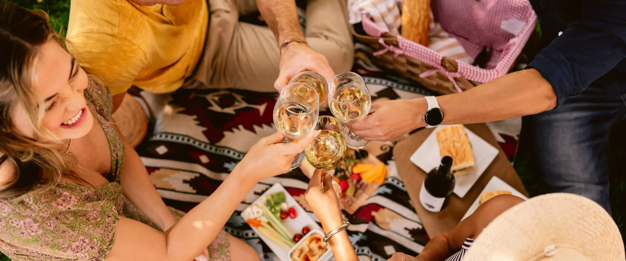 Group of friends enjoy wine and charcuterie on a blanket.